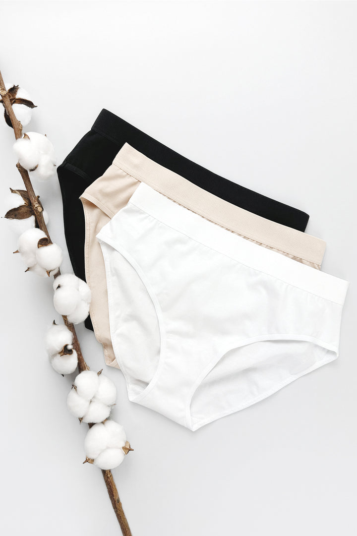 Three-pack of 100% cotton panties in black, beige, and white with elastic waistbands, cotton crotches, and classic fit
